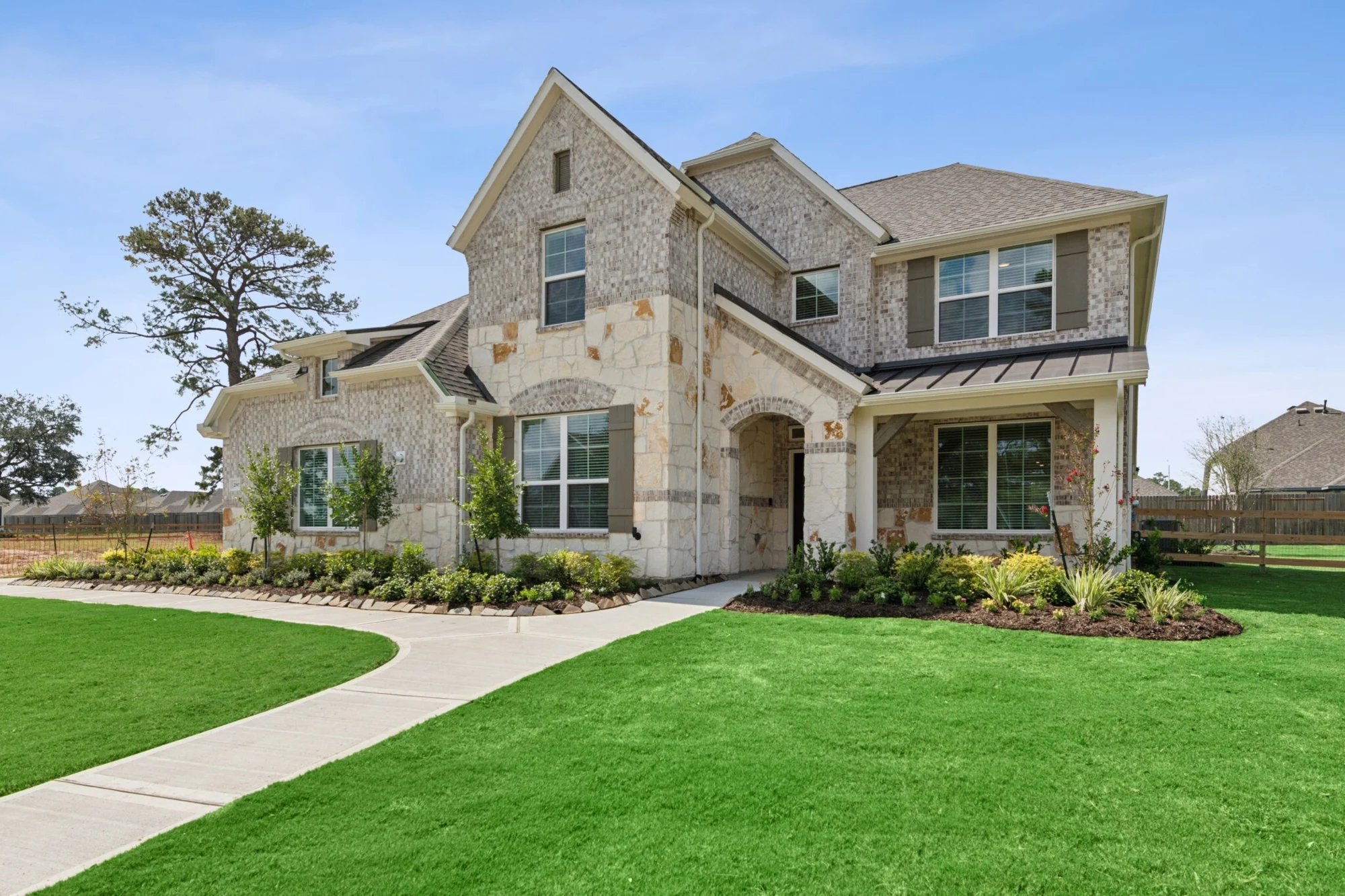 Two-story brick-and-stone new-construction home with an arched entry, gabled roof and landscaped beds