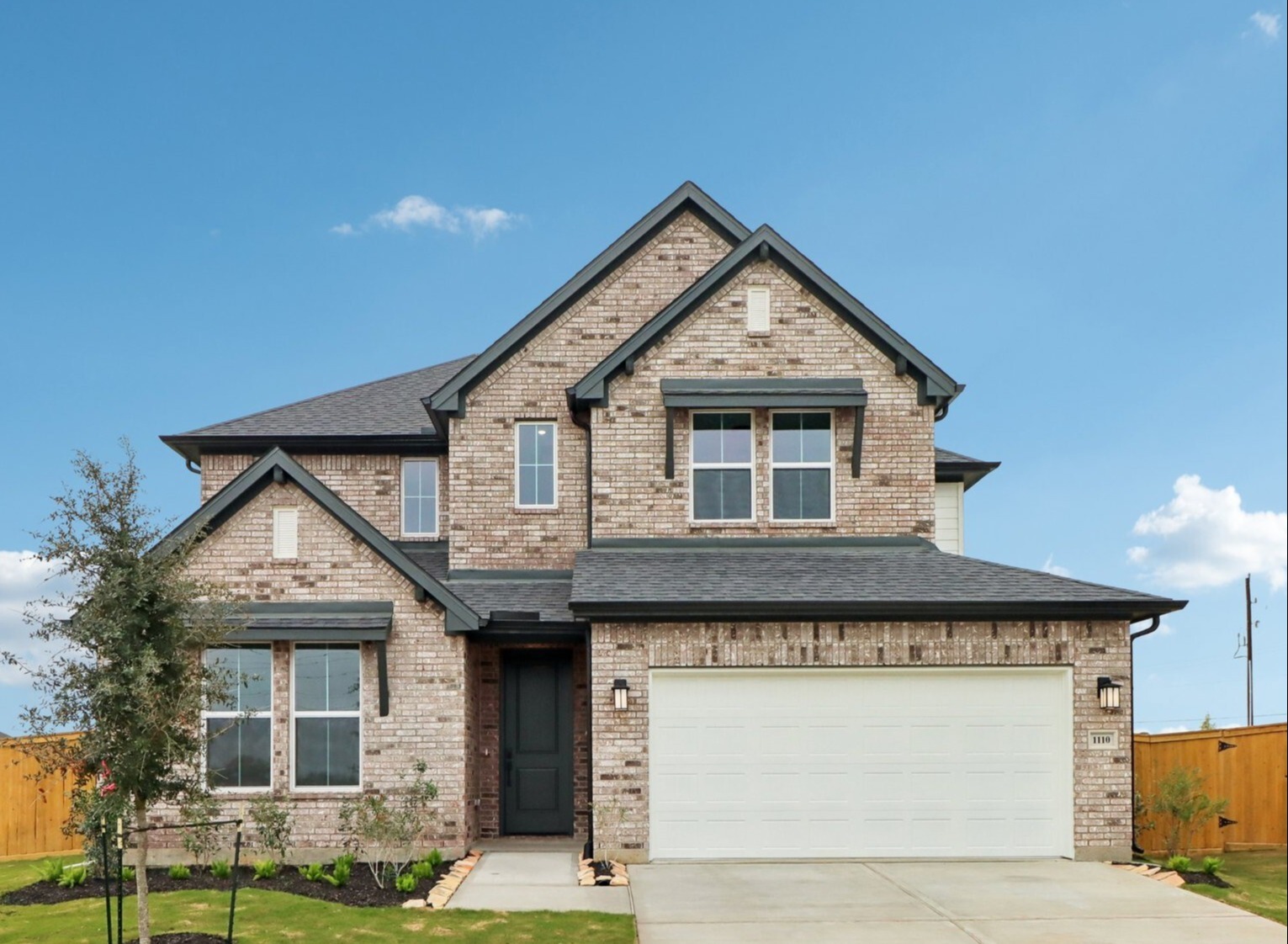 Two-storey brick new-construction home with multiple gable roofs, dark shutters and a two-car garage