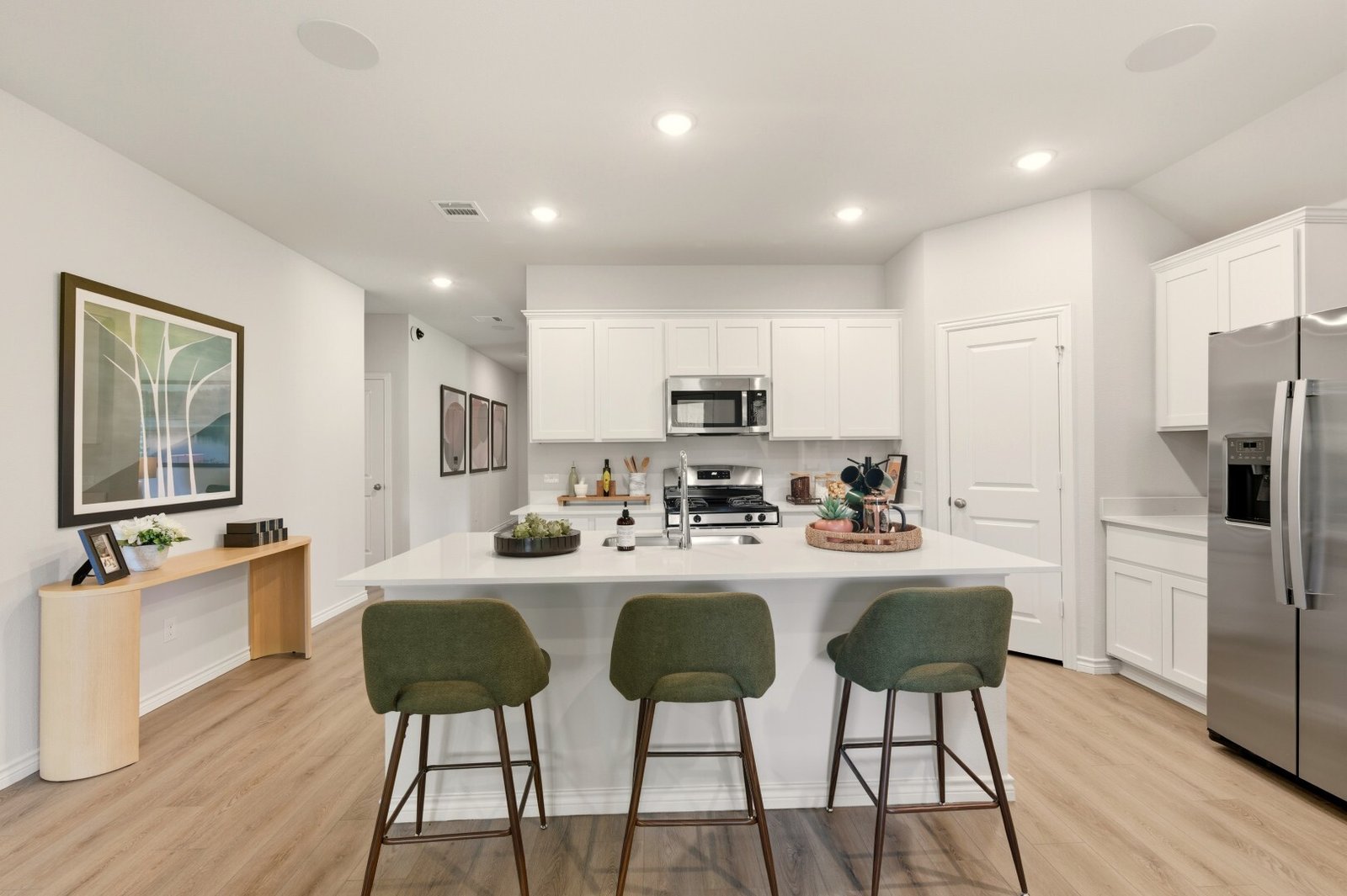 Kitchen island in white quartz with three green upholstered bar stools, white shaker cabinets and stainless appliances