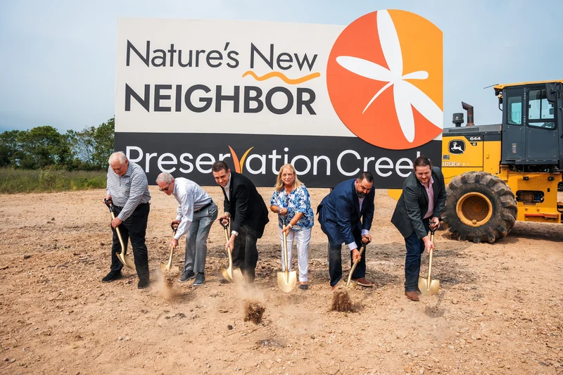 Groundbreaking: six people turning soil with gold shovels before the Nature's New Neighbor Preservation Creek sign
