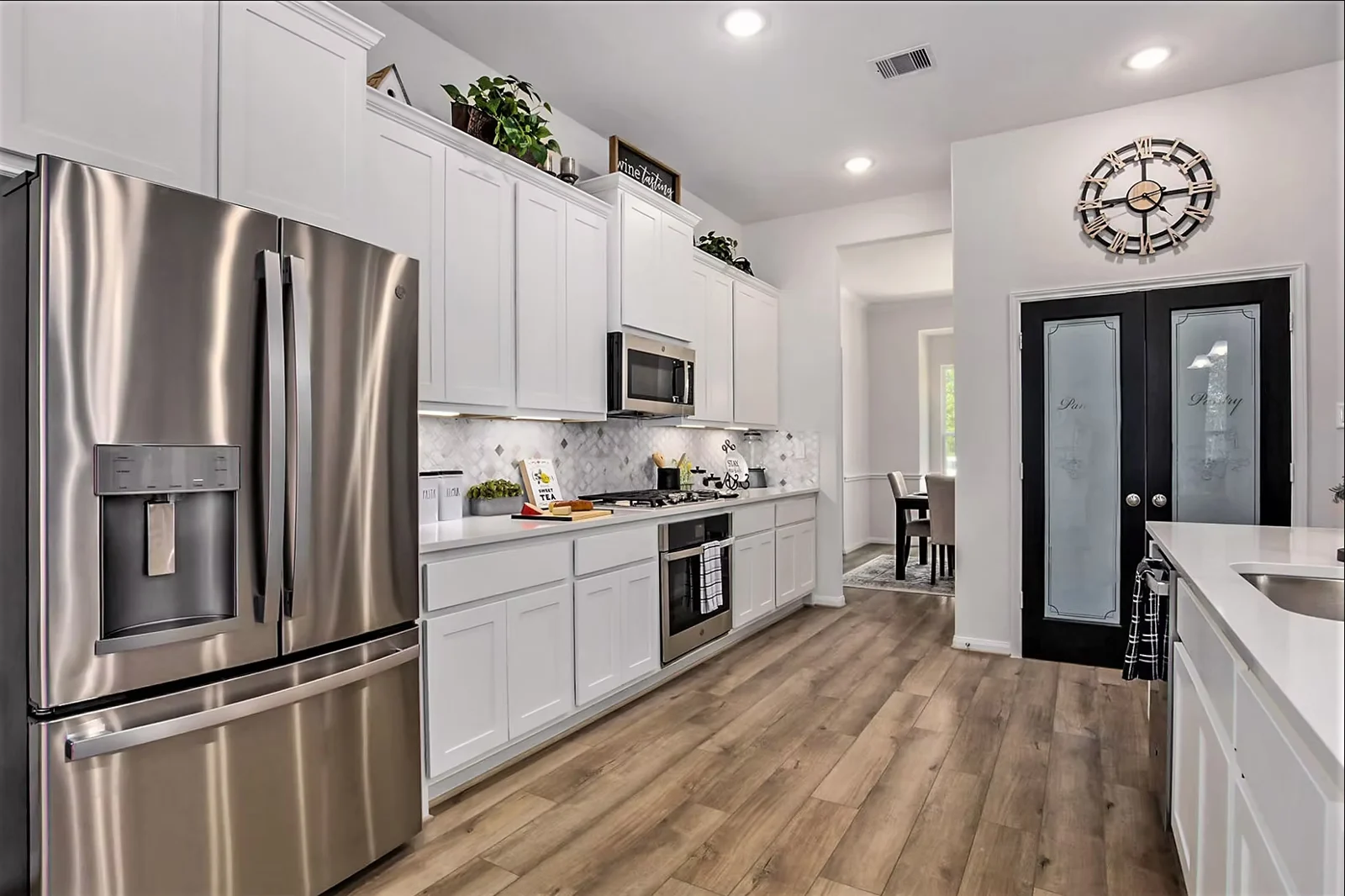 Kitchen with white shaker cabinets, a stainless refrigerator, wall oven and glass pantry doors