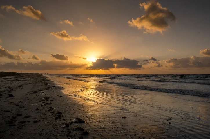 Sun setting over a Gulf Coast shoreline with clouds above the water