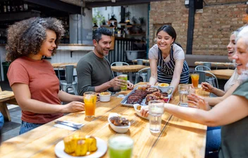 Server bringing a tray of barbecue to four people at a restaurant table