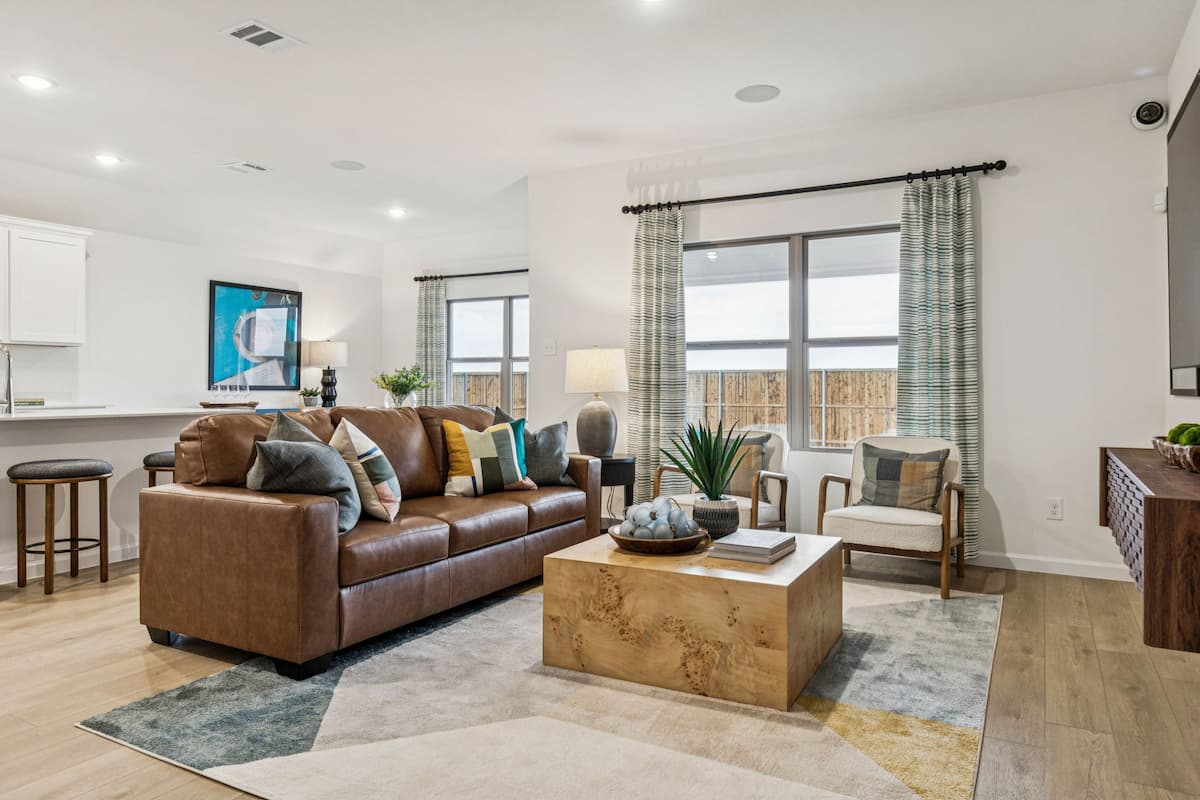 Living room with a brown leather sofa, burl-wood coffee table and striped curtains, open to the kitchen