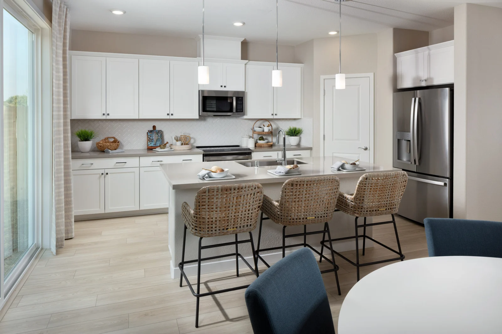 RiseWell Homes model home kitchen with white cabinets, a quartz island and three barstools