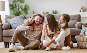 Family of four sitting together on the floor in front of a sofa, laughing