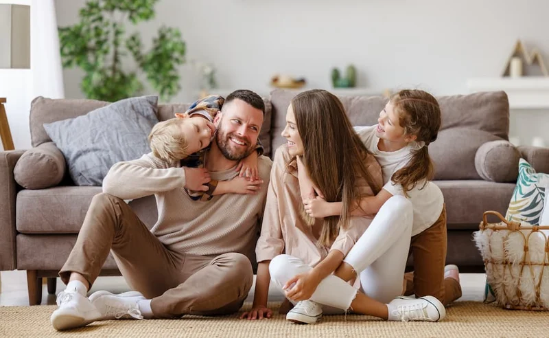 Family of four sitting together on the floor in front of a sofa, laughing