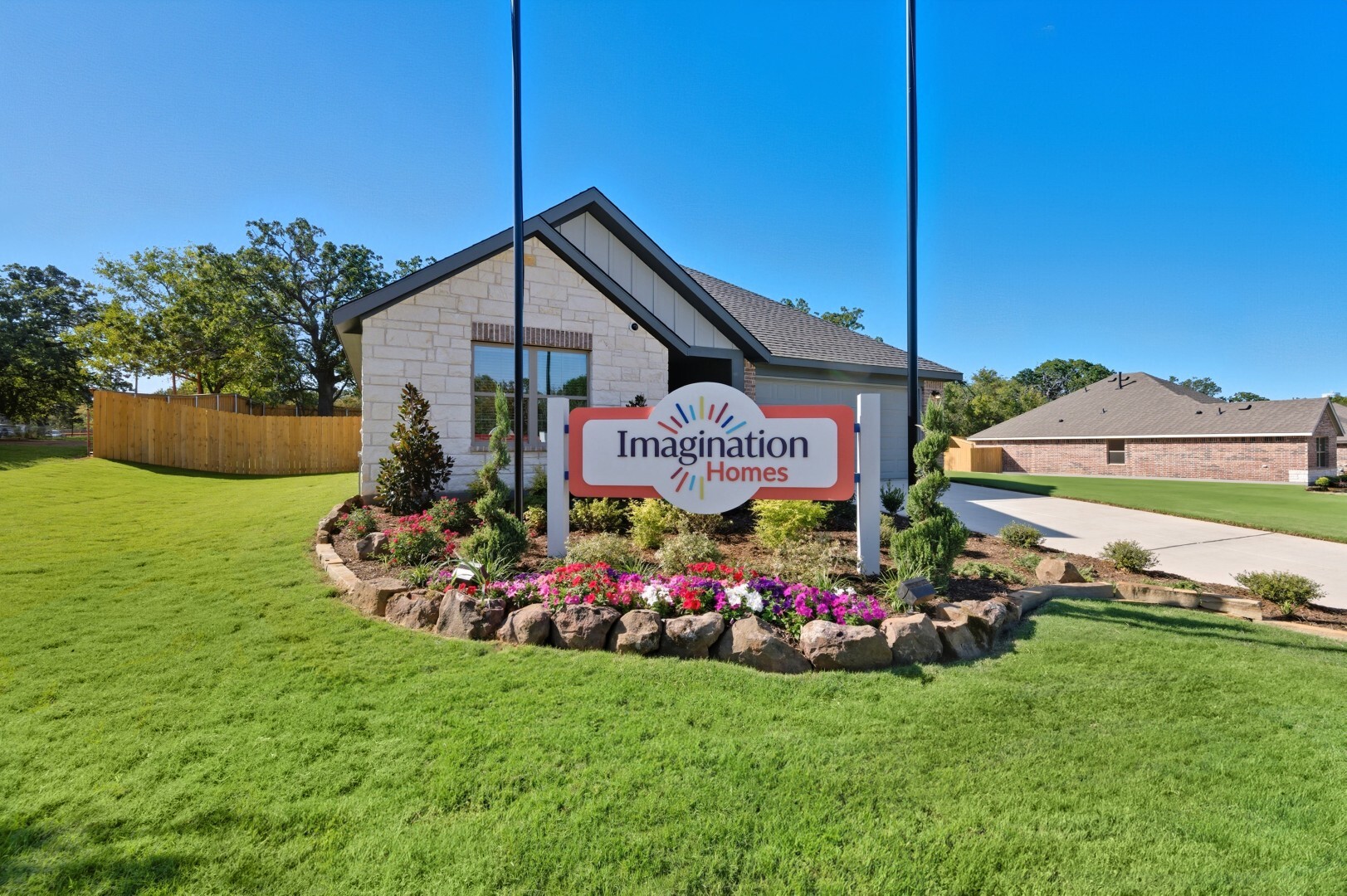 Imagination Homes sign on a landscaped flower bed in front of a single-story stone and board-and-batten model home