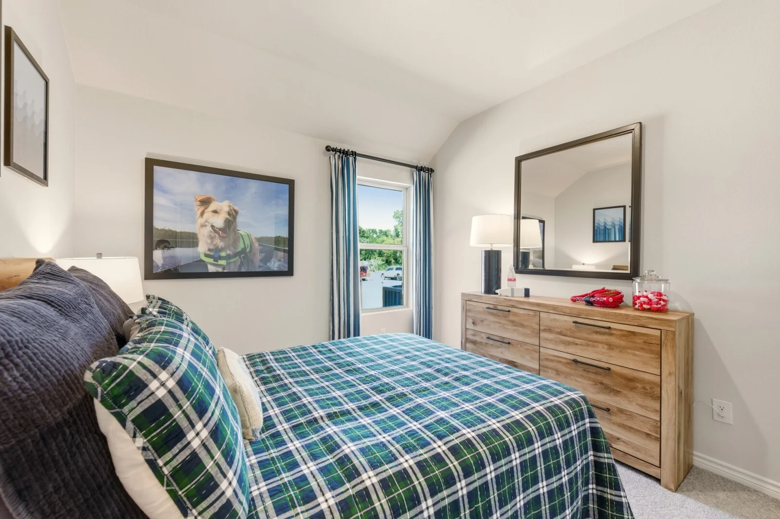 Secondary bedroom with plaid bedding, a wood dresser and mirror, and framed dog photography