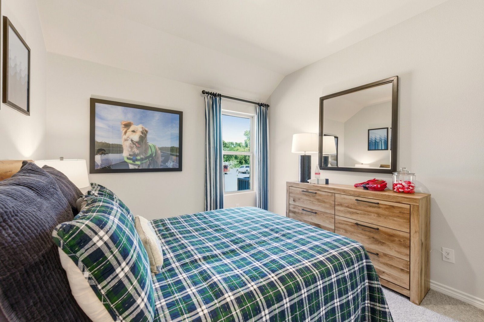 Secondary bedroom with plaid bedding, a wood dresser and mirror, and framed dog photography