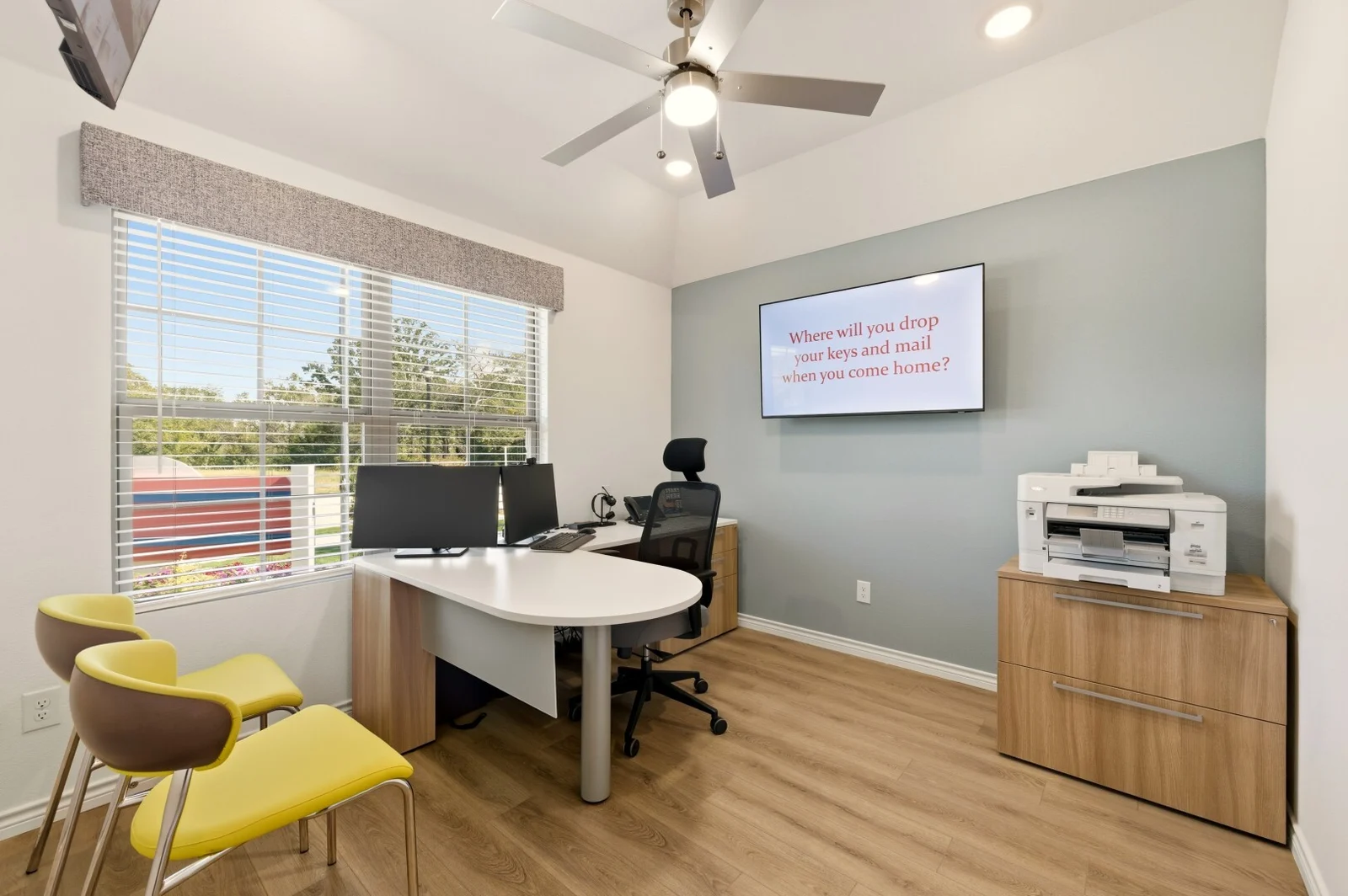 Sales office desk with dual monitors and a screen reading 'Where will you drop your keys and mail when you come home?'