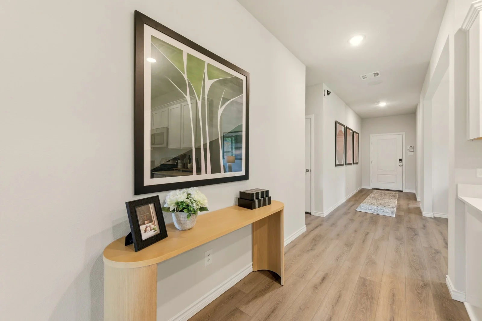 Entry hallway with framed tree artwork above a curved console table, looking toward the front door