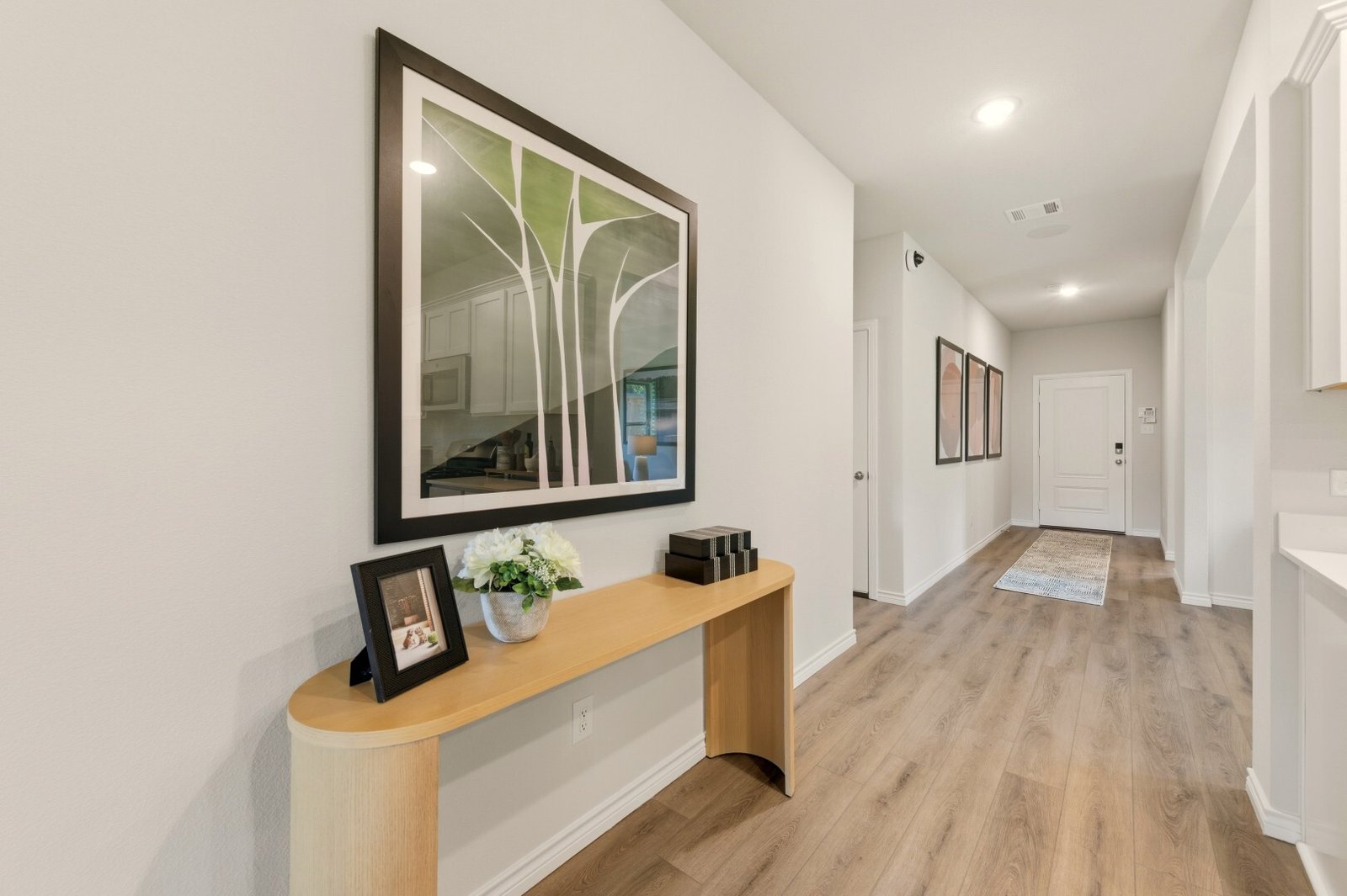 Entry hallway with framed tree artwork above a curved console table, looking toward the front door