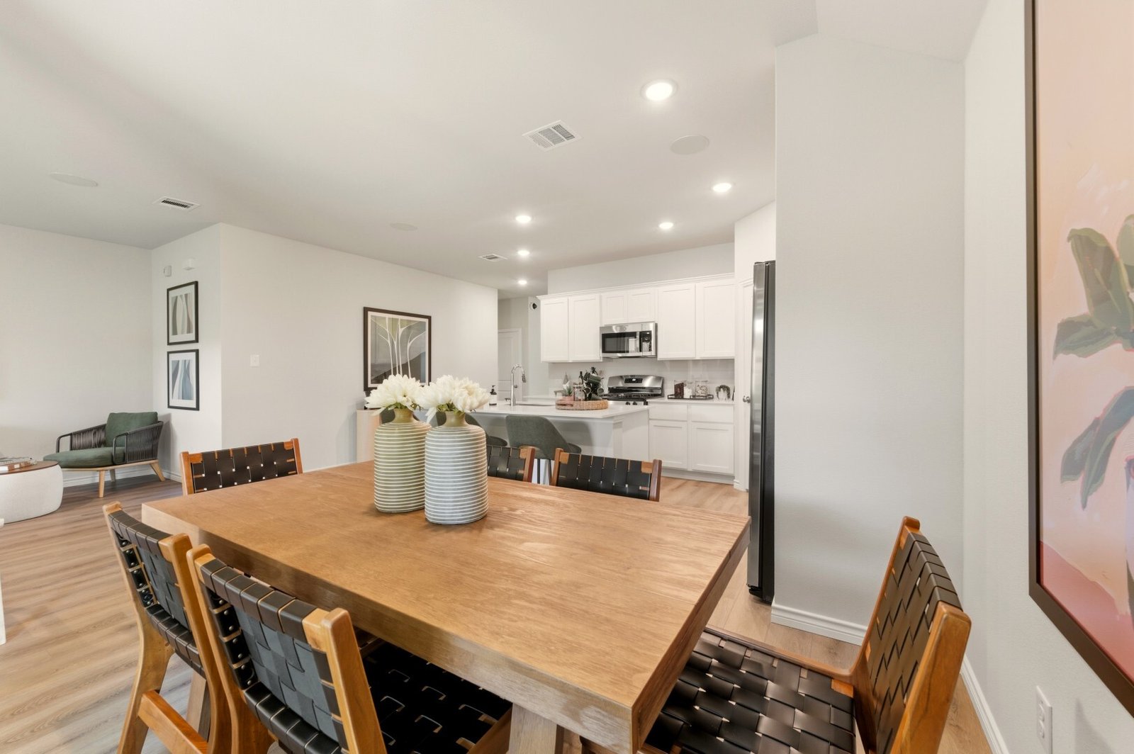 Dining area with a wood table and woven leather chairs, open to a white kitchen and the living room beyond