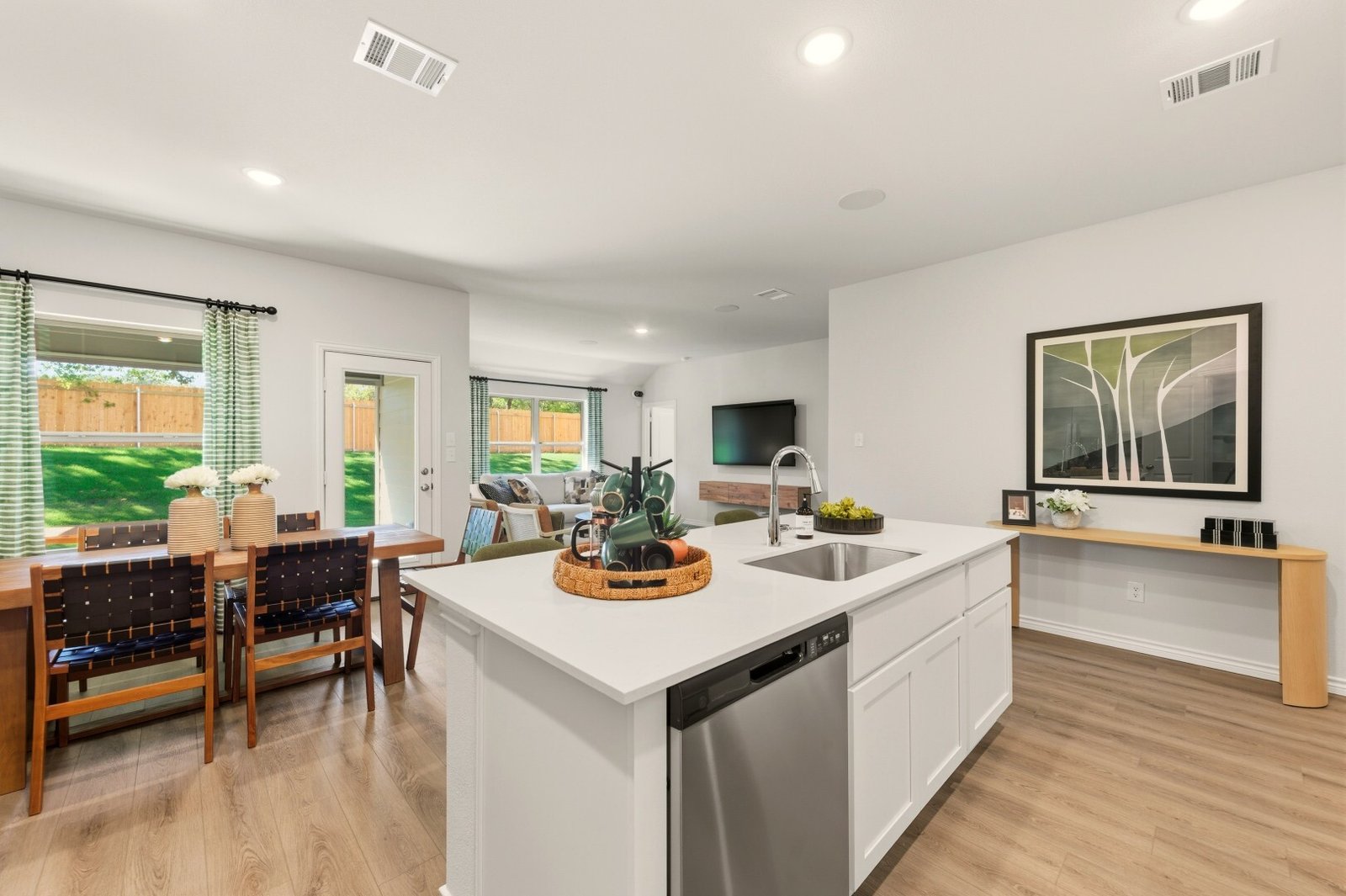 Kitchen island with a sink and dishwasher, open to a dining area and a living room with a wall-mounted TV