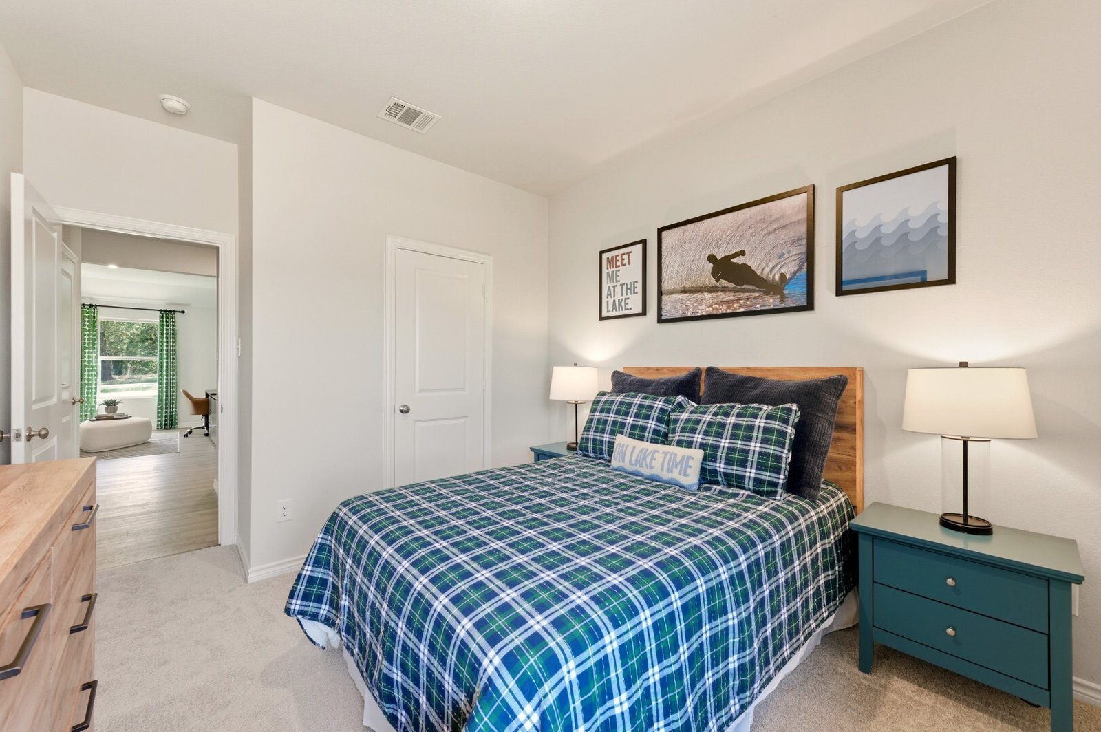 Secondary bedroom with plaid bedding, teal nightstands and lake-themed wall art, opening onto a study