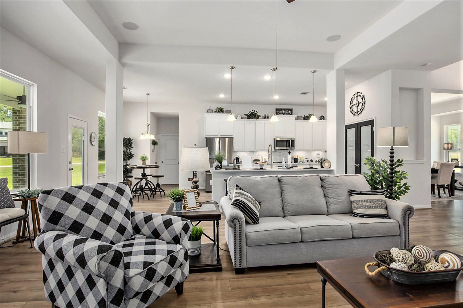 Kendall Homes model home open-plan living room and kitchen with a grey sofa and buffalo-check armchair