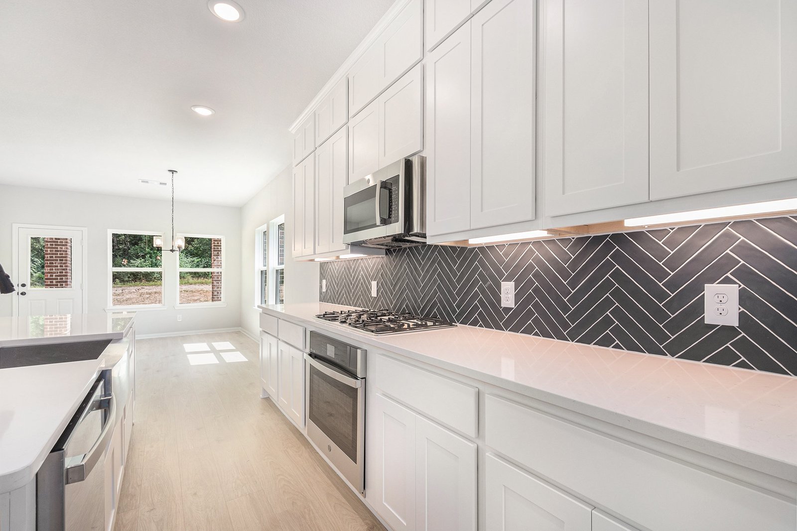Kendall Homes model home galley kitchen with white shaker cabinets, quartz worktops and a dark herringbone tile splashback