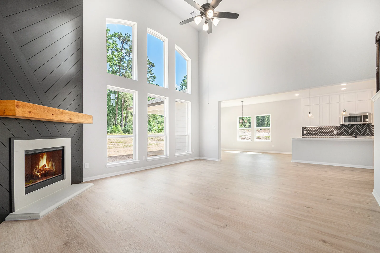 Living room with a dark chevron shiplap fireplace wall, wood mantel and two-story arched windows, open to the kitchen