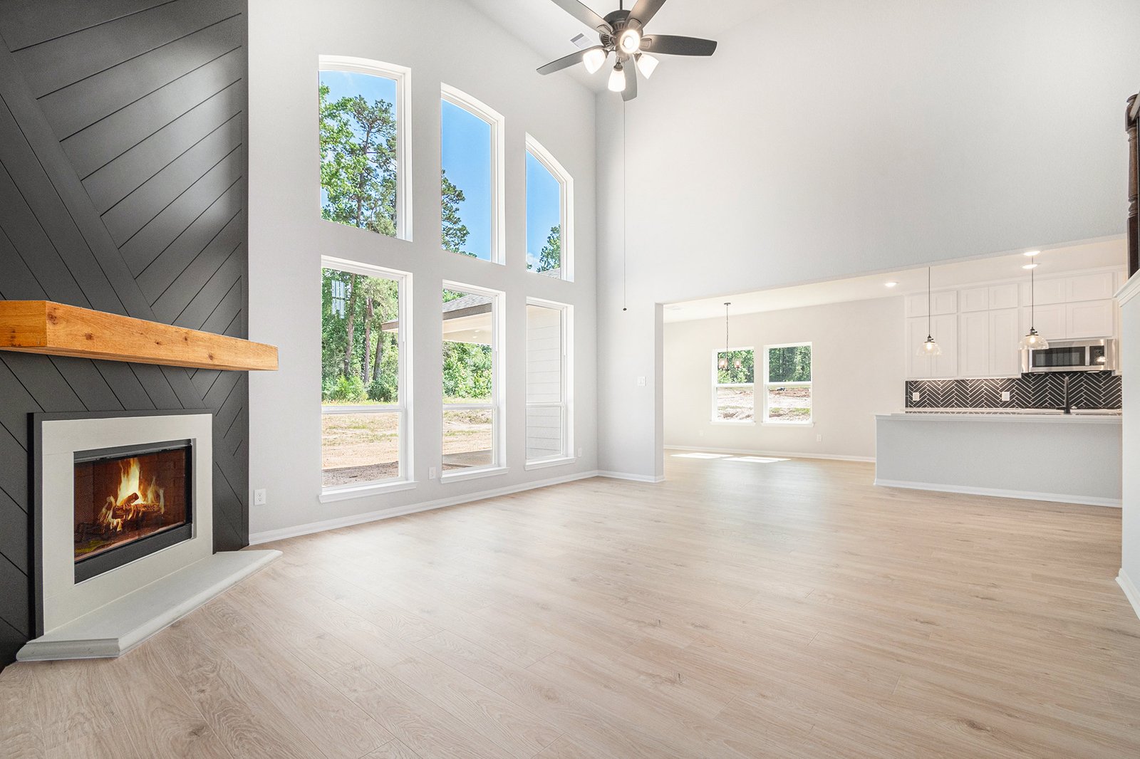 Living room with a dark chevron shiplap fireplace wall, timber mantel and two-storey arched windows, open to the kitchen