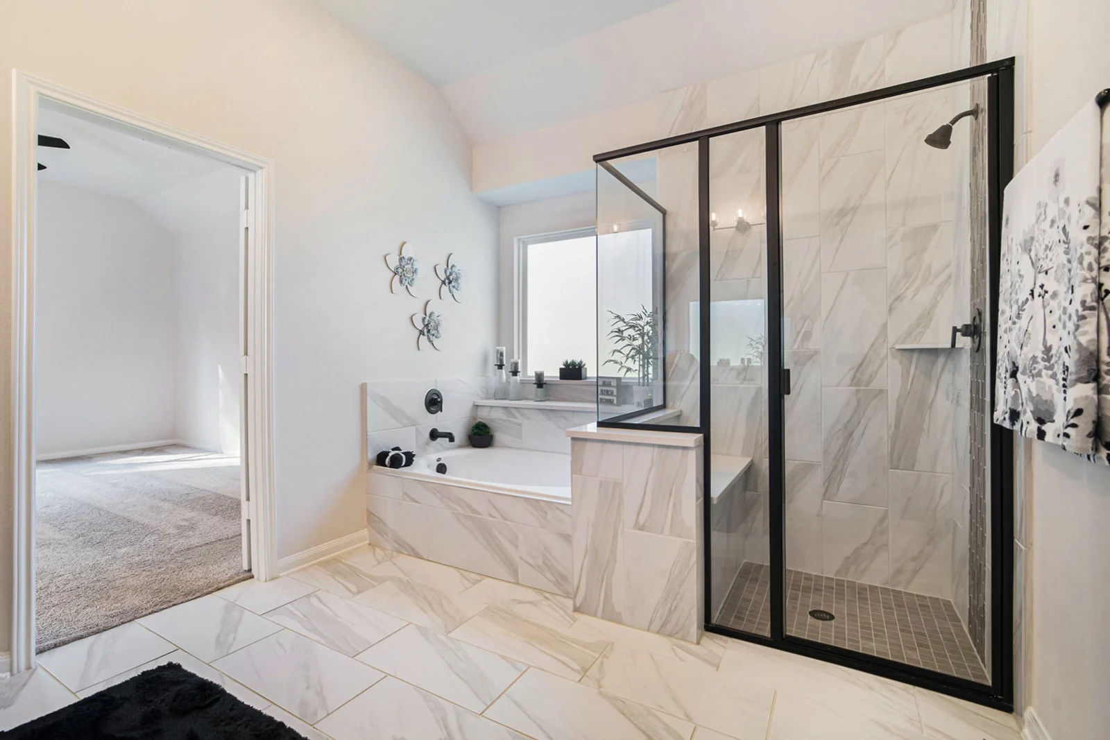 Kendall Homes model home primary bathroom with a marble-look tiled tub and a black-framed glass shower