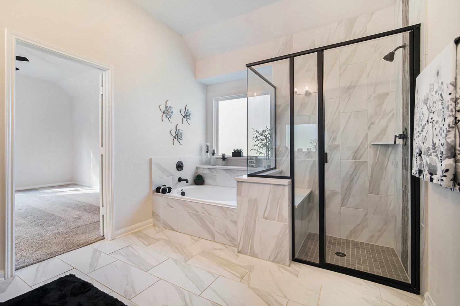 Kendall Homes model home primary bathroom with a marble-look tiled tub and a black-framed glass shower