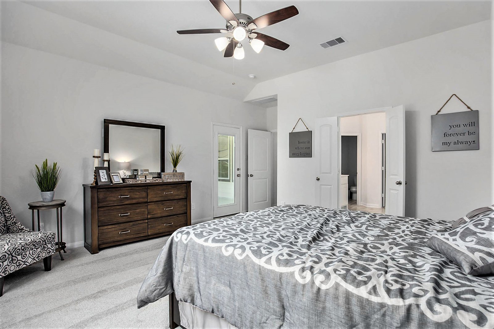 Kendall Homes model home primary bedroom with a vaulted ceiling, dark wood dresser and an en-suite beyond