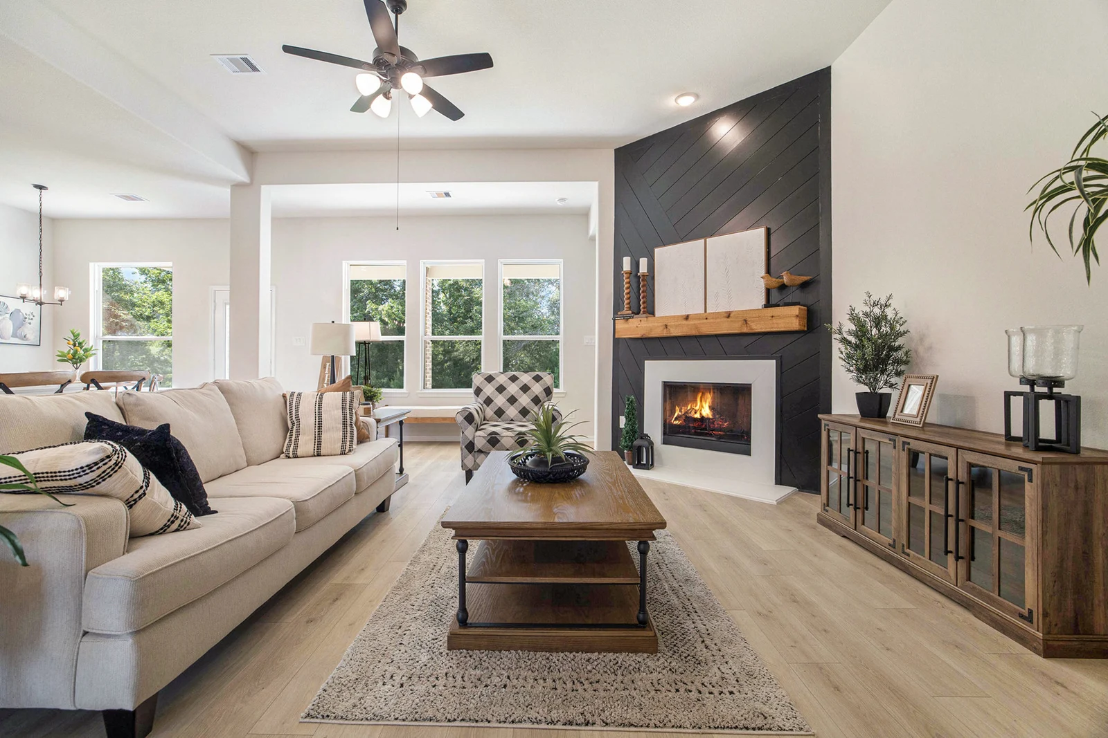 Model home living room with a dark chevron shiplap fireplace wall, wood mantel and a plaid armchair
