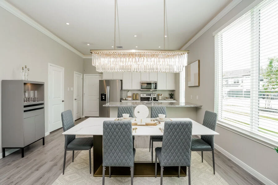 Dining area with a marble-top table, gray quilted chairs and a linear crystal chandelier, open to the kitchen
