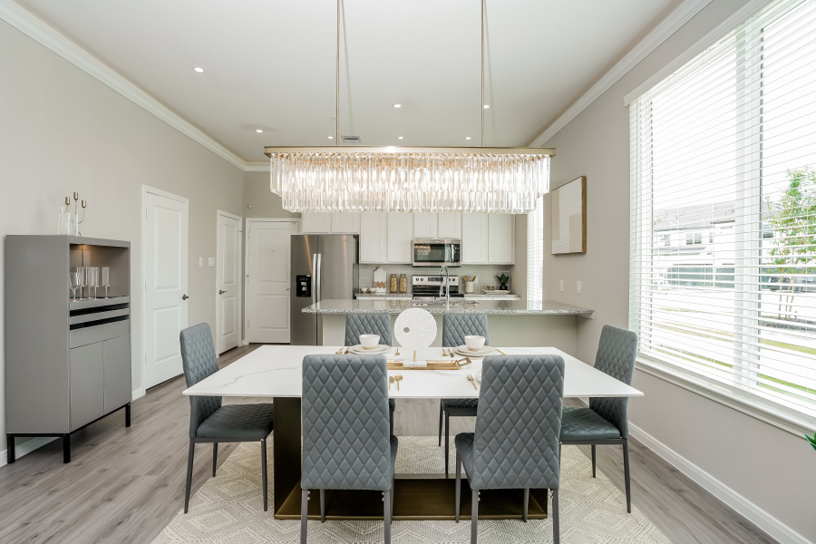 Dining area with a marble-top table, grey quilted chairs and a linear crystal chandelier, open to the kitchen