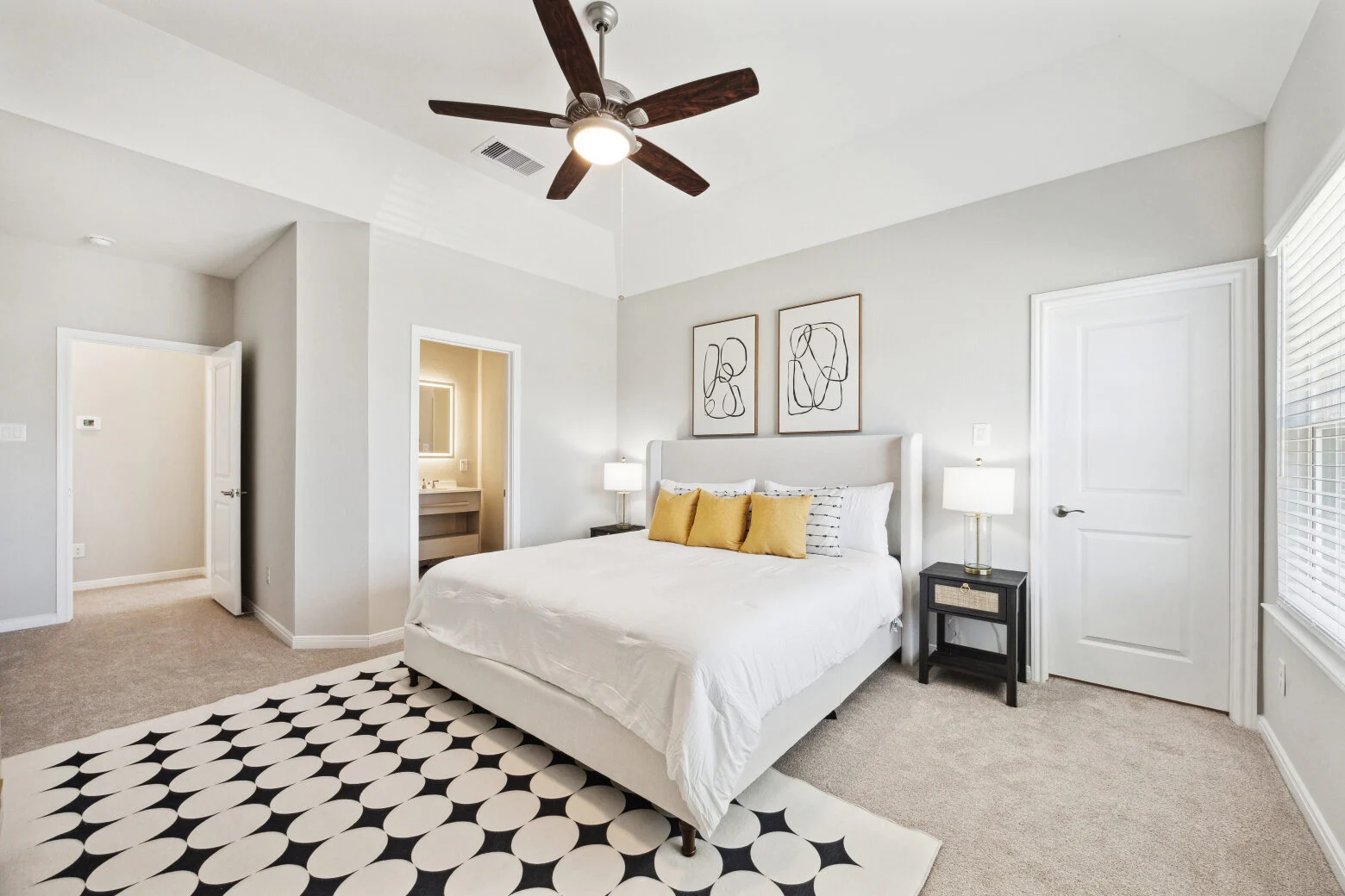 Primary bedroom with an upholstered wing bed, mustard pillows, line-drawing prints and an en-suite doorway