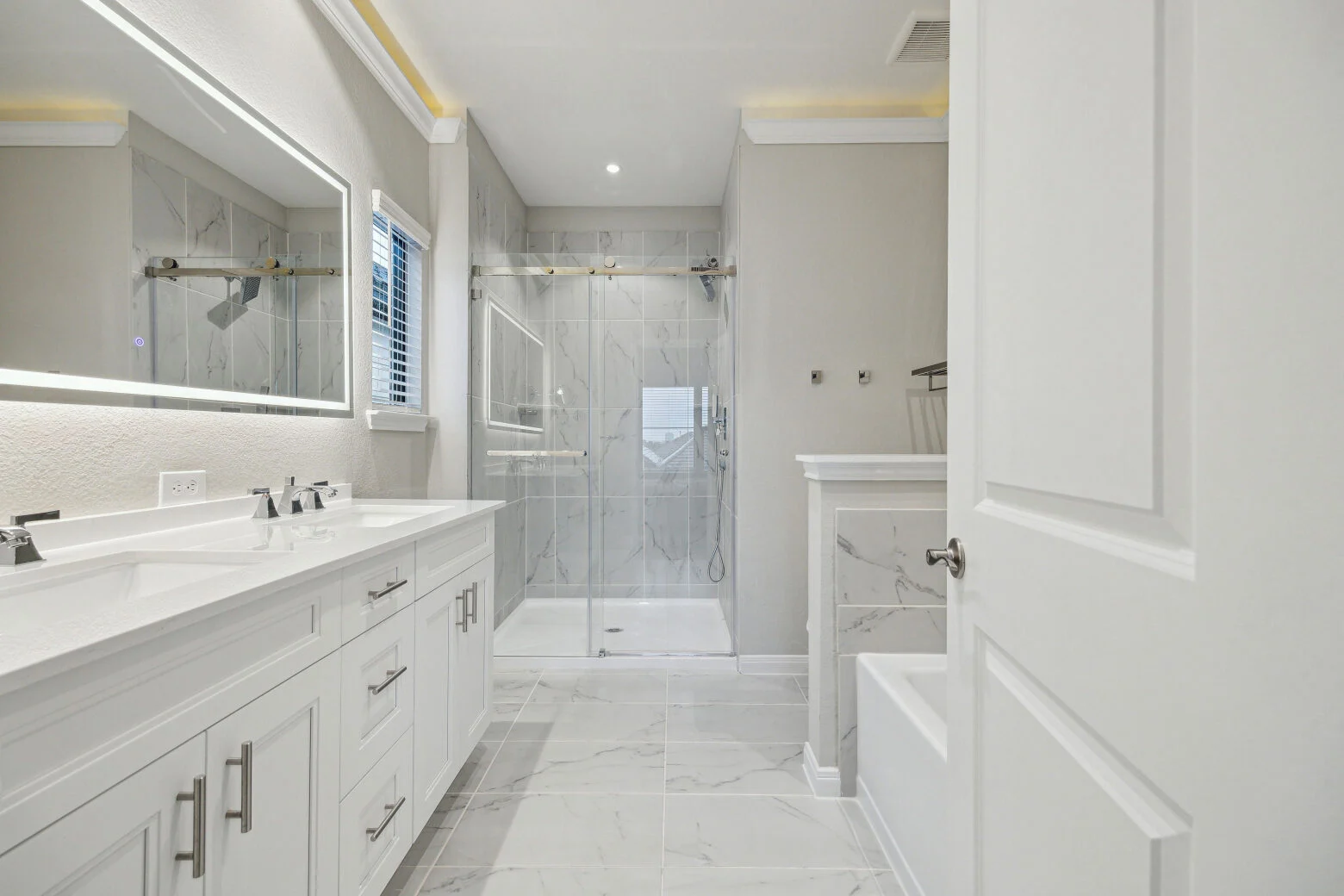Bathroom with a double vanity, backlit mirror, marble-look walk-in shower and a separate tub