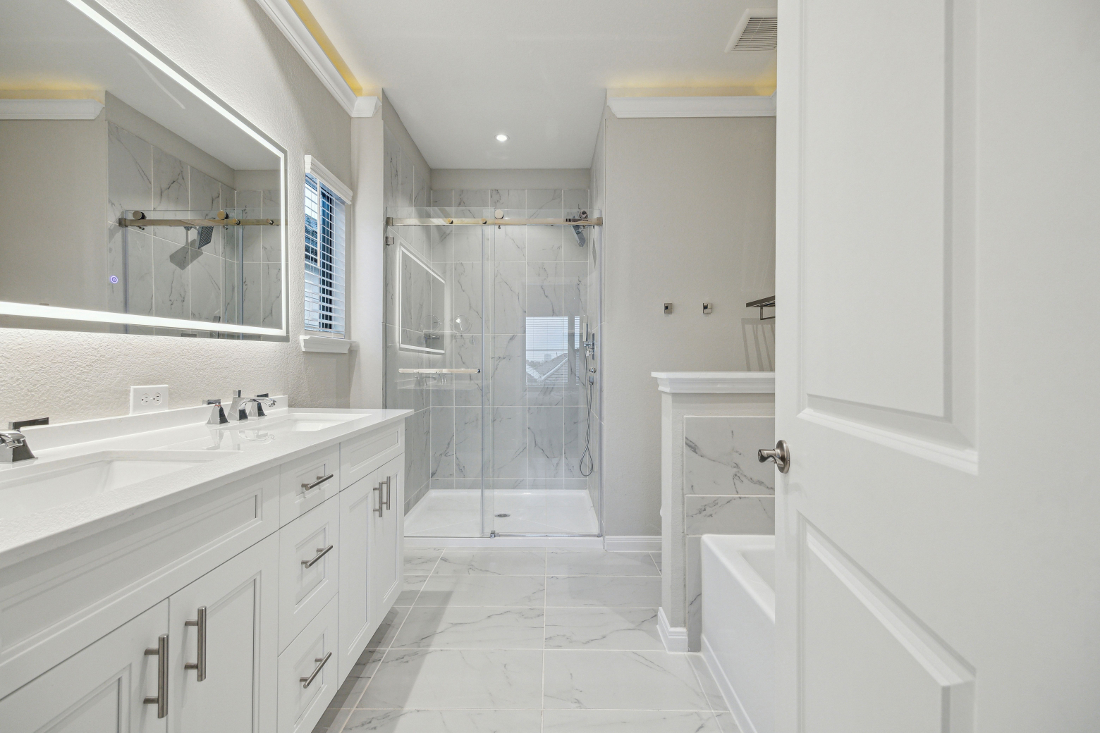 Bathroom with a double vanity, backlit mirror, marble-look walk-in shower and a separate tub