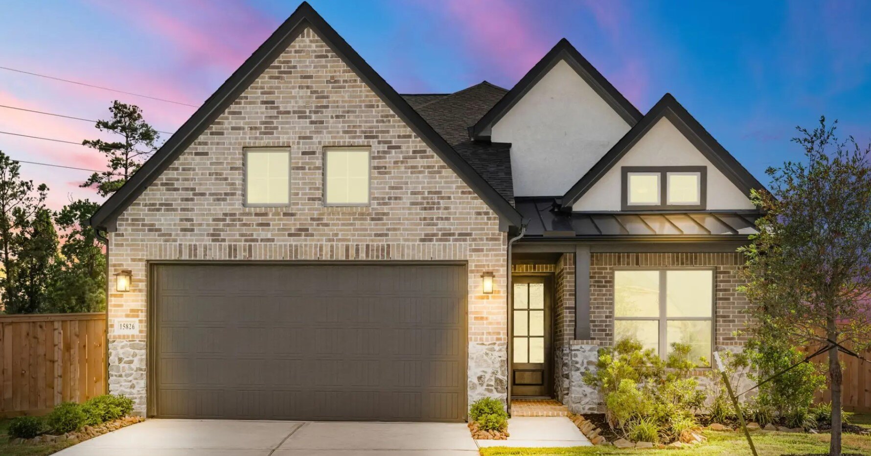Two-story brick and stone home exterior at dusk with lit windows