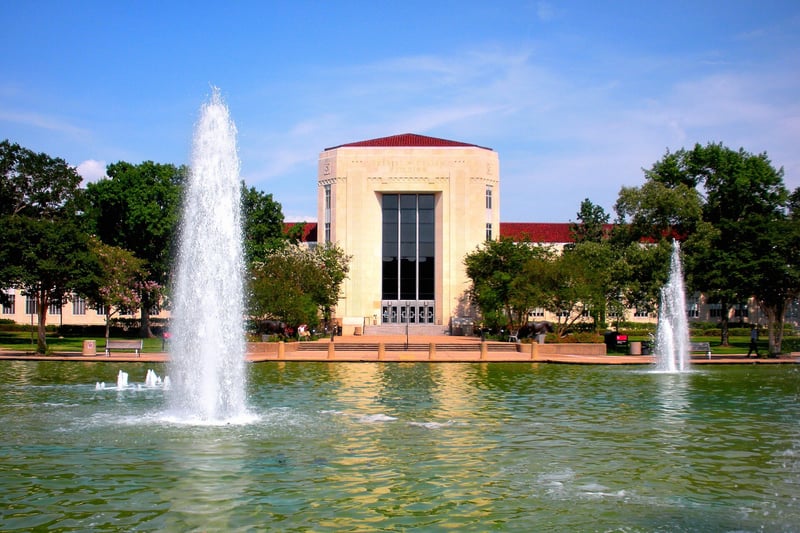 Fountains in front of a limestone university building with a red-tiled roof