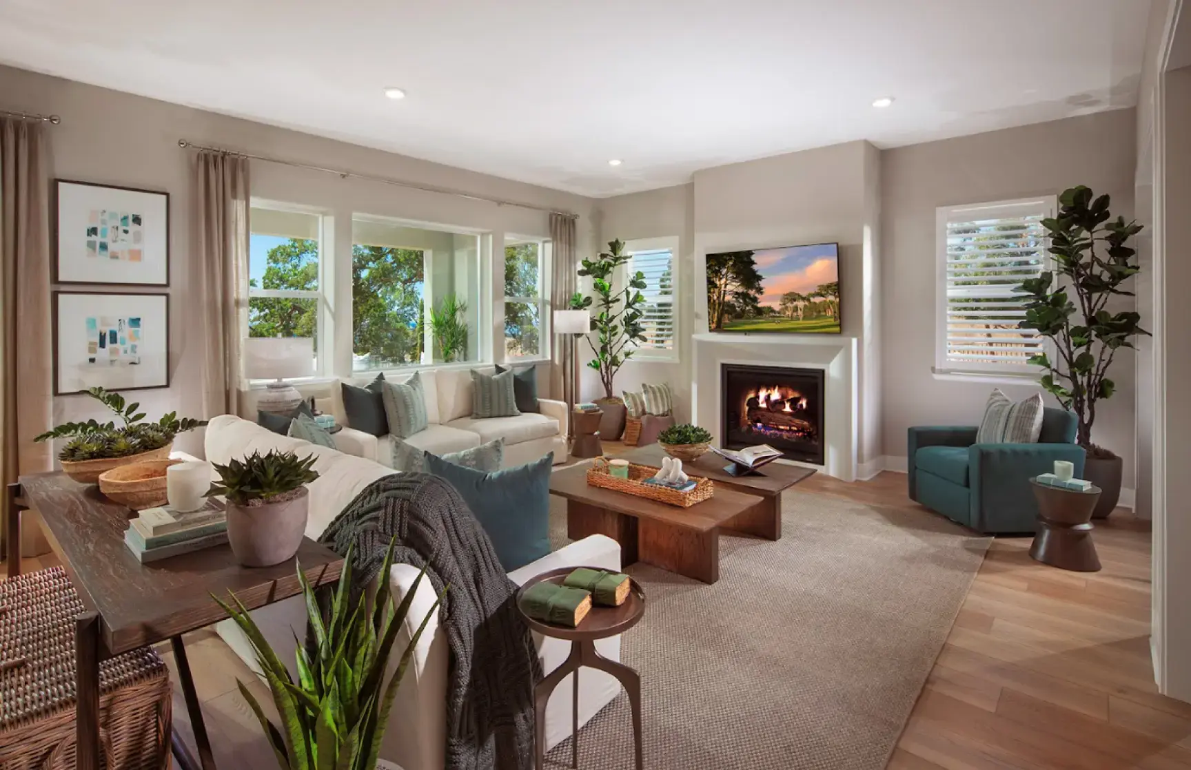 RiseWell Homes model home living room with a wall-mounted TV above the fireplace and windows overlooking mature trees